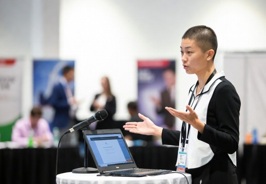 A speaker presenting beside a laptop at a conference